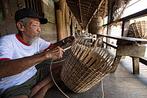 Village chief Apai Bandi weaving basket on the front porch of longhouse, Iban tribe of Dayak people, Kapuas Ulu, Kalimantan, Borneo, Indonesia.
