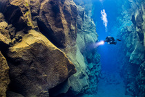 Diver swimming through the Silfra fissure, a crack in the Earth's crust between the North American and Eurasian continental plates, which is filled with glacial melt water, Thingvellir National P...