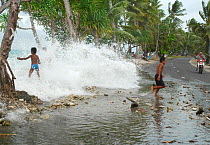 Children playing in waves washing onto a road during high tides of February 2005 that inundated part of Funafuti, Tuvalu, Pacific Ocean. February, 2005.