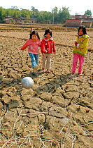 Three children playing football in dried up rice fields after severe drought, Fu Lou Village, Guangdong, China. January, 2005.