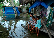 Children sitting on their "kaupapa," the outdoor sleeping platform favored by Tuvaluan families, surrounded by very high tide water, Tuvalu. February 9th, 2005. Small repro only.