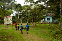 People walking past sign and guest house, Cinchona Forest Reserve Station, Kitanglad Range Natural Park, Mindanao, Philippines, February 2007.