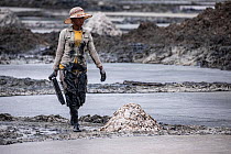 Woman working at Lake Katwe salt works, Queen Elizabeth National Park, Uganda. February, 2023. Saline water is evaporated from dug earthen ponds to produce rock salt and 'muddy' salt used fo...
