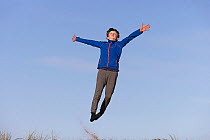 Boy jumping for joy over sand dune, Winterton Dunes National Nature Reserve, Norfolk, England, UK. February, 2022. Model released.