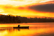 Man paddling Canadian canoe over Lake Windermere at sunrise, Ambleside, Lake District, Cumbria, UK, December 2014.