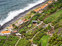 View looking down on cable car on steep coastal cliffs with an organic farm at bottom, Faja dos Padres, Madeira. March, 2023.