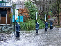 Electric car charging points submerged in water in a flooded carpark after heavy rain, Ambleside, Lake District, Cumbria, UK. January, 2023.