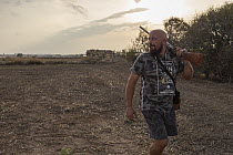 Maltese hunter walking through farmland at dawn with shotgun, looking for Common quail (Coturnix coturnix), Siggiewi, Malta. September, 2020. Model released.