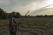 Maltese hunter standing with shotgun in farmland at dawn, watching for Common quail (Coturnix coturnix), Siggiewi, Malta, September, 2020. Model released.