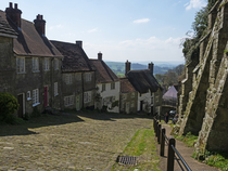 View down the steep cobbled street of Gold Hill lined with houses and the buttressed walls of the Precinct part of the ancient Shaftesbury Abbey, Dorset, England, UK. April, 2023.