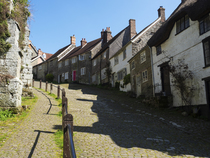View up the steep cobbled street of Gold Hill lined with houses and the buttressed walls of the Precinct part of the ancient Shaftesbury Abbey, Dorset, England, UK. April, 2023.