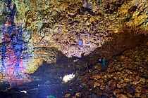 Tourists looking at colourful rocks inside the magma chamber of Thrihnukagigur volcano, a dormant volcano now used for tours. Yellow is sulfur oxide, grey and black is basalt rock and green is copper....