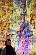 Tourist looking at colourful rocks inside the magma chamber of Thrihnukagigur volcano, a dormant volcano now used for tours. Yellow is sulfur oxide, grey and black is basalt rock and green is copper....