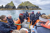 Group of people on boat taking part in the release of European lobster (Homarus gammarus) juveniles into the sea, National Lobster Hatchery, Padstow, Cornwall, UK. July, 2023.