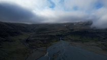 Drone shot of dry glacial river. The drone descends below the clouds and mountains and then the river is revealed. South Iceland. June.