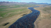 Aerial shot of braided glacial river. The drone pans up and reveals mountains. Iceland. June.