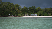 Tracking shot of small settlement on sandy beach surrounded by dense forest. The sky is dark and rain clouds are approaching fast. Island north of New Ireland, Papua New Guinea.