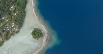 Aerial tracking shot of the coastline, including reef, sandy beach, coastal community and forest, Murat LLG, New Ireland, Papua New Guinea.