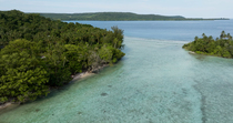 Drone tracking shot through water channel between two islands. A small settlement is visible at the shore of the island on the left. Murat LLG, New Ireland, Papua New Guinea.