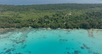Drone tracking shot of ocean with visable coral reef pinnacles and houses on forested island, New Ireland, Papua New Guinea.