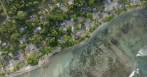 Aerial shot of a coastal community and adjacent ocean with visible coral reef pinnacles, Papua New Guinea.