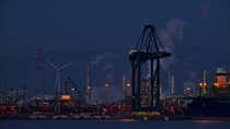 Container terminal at night, showing wharf with stacked containers, gantry crane and wind turbine along the Western Scheldt, Port of Antwerp, Flanders, Belgium. 2023.