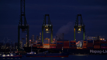 Container terminal at night, showing ship stacked with containers and gantry cranes behind, along the Western Scheldt, Port of Antwerp, Flanders, Belgium. 2023.