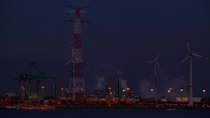 Container terminal at night, showing wharf with electricity pylon, gantry crane and wind turbines along the Western Scheldt, Port of Antwerp, Flanders, Belgium. 2023.