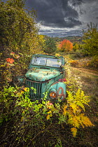 Abandoned old Soviet era truck surrounded by autumn foliage under stormy sky, Rhodpe Mountains, Bulgaria. October, 2023.
