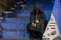 Local man sitting on steps smoking an hashish pipe, northern Morocco. January, 2024.