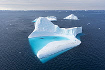 Aerial view of group of Adelie penguins (Pygoscelis adeliae) standing on a large iceberg alongside a turquoise pool, Weddell Sea, Antarctica.
