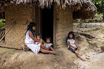 Woman with her children sitting outside village hut, El Encanto, Sierra Nevada de Santa Marta, Colombia. December, 2021.