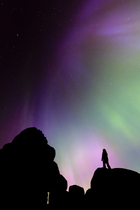 Aurora borealis in night sky with person silhouetted on Robin Hood's Stride rock formation, Peak District National Park, Derbyshire, England, UK. 10th May 2024.