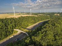 Aerial view of a wildlife crossing over the A7 highway, built in 2011, with wind turbines in distance, Drome, France. June, 2018.