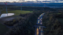 Aerial view of a wildlife crossing over the A7 highway at dusk, built in 2011, with wind turbines along the highway and city of Salaise-sur-Sanne in the distance, Drome, France. November, 2023.
