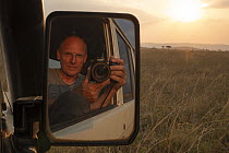 Photographer, Klaus Nigge, taking photographs from car at sunset, reflection in car wing mirror, Serengeti National Park Tanzania. September, 2017.