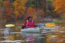 Woman kayaking on lake surrounded by autumnal trees, Maryland, USA. October, 2023.