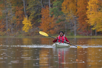 Woman kayaking on lake surrounded by autumnal trees, Maryland, USA. October, 2023.