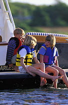 Children wearing lifejackets on the transom of a Little Harbor Whisper powerboat, paddling and chatting, Rhode Island, USA.