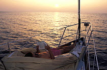 Man laying on a folded kevlar sail whilst reading at sunset