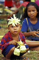 Young boy wearing palm leaf headdress and decorations for traditional feast, with young girl behind, Yap, Micronesia.