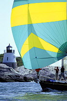 The crew of a Morris 46 gybe the spinnaker in front of the Castle Hill Lighthouse which marks the East Passage into Narragansett Bay, Newport, Rhode Island, USA.