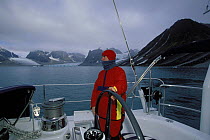 Man at the helm steering 88ft sloop "Shaman", in a fjord. Spitsbergen, Svalbard, Norway, 1998.