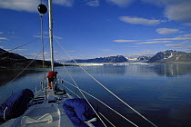 Man preparing to anchor aboard 88ft sloop  "Shaman" with Spitsbergen's mountains and glaciers in the background on a calm day. Svalbard Archipelago, Norway, 1998.