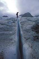 Person peering into the depths of a narrow crevasse on glacier, Spitsbergen, Svalbard, Norway, 1998.
