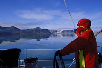 Woman in warm clothing steering 88ft sloop "Shaman" through the islands of Spitsbergen, Svalbard, Norway, summer of 1998.