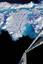 Crew member standing on the bow of 88ft sloop "Shaman" to communicate with the skipper when approaching a large iceberg Spitsbergen, viewed from the masthead. Svalbard, Norway 1998.
