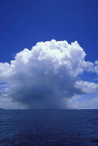 Thunder cloud and rain squall over the ocean, with a small yacht.