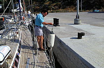 Man with fender, mooring a yacht to the harbour wall in Greece.