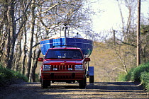 A yacht being transported overland on a trailer pulled by a red jeep, Cape Cod, Massachusetts, USA.
